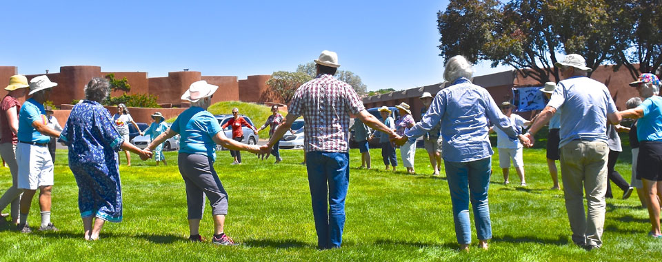 Community members holding hands standing in a circle on grass, celebrating 50th Anniversary La Luz 50th Anniversary Community Celebration